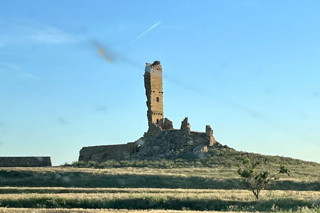Die steinernen Überreste eines einsamen, hohen Gebäudes auf einem grasbewachsenen Hügel in Aragonien unter blauem Himmel.