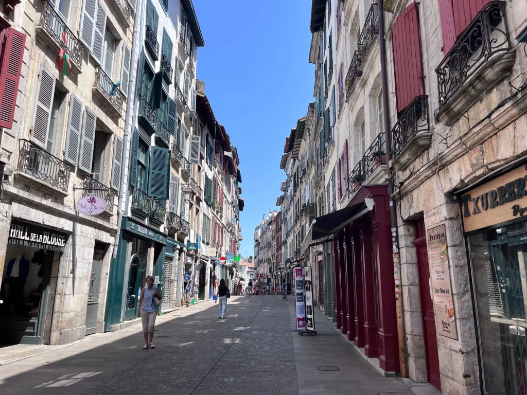 Eine enge, sonnige Gasse mit traditionellen baskischen Häusern mit roten und grünen Fensterläden in der Altstadt von Saint-Jean-de-Luz.