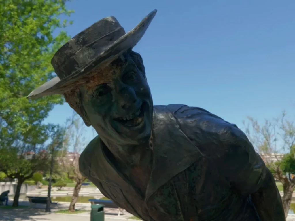 Nahaufnahme der bronzenen Statue des berühmten spanischen Clowns Pepe Tonetti im Parque de Mesones in Santander. Die Skulptur zeigt das lachende Gesicht des Clowns mit einem Hut, der sich verschmitzt nach vorne beugt. Im Hintergrund ist ein blauer Himmel zu sehen.