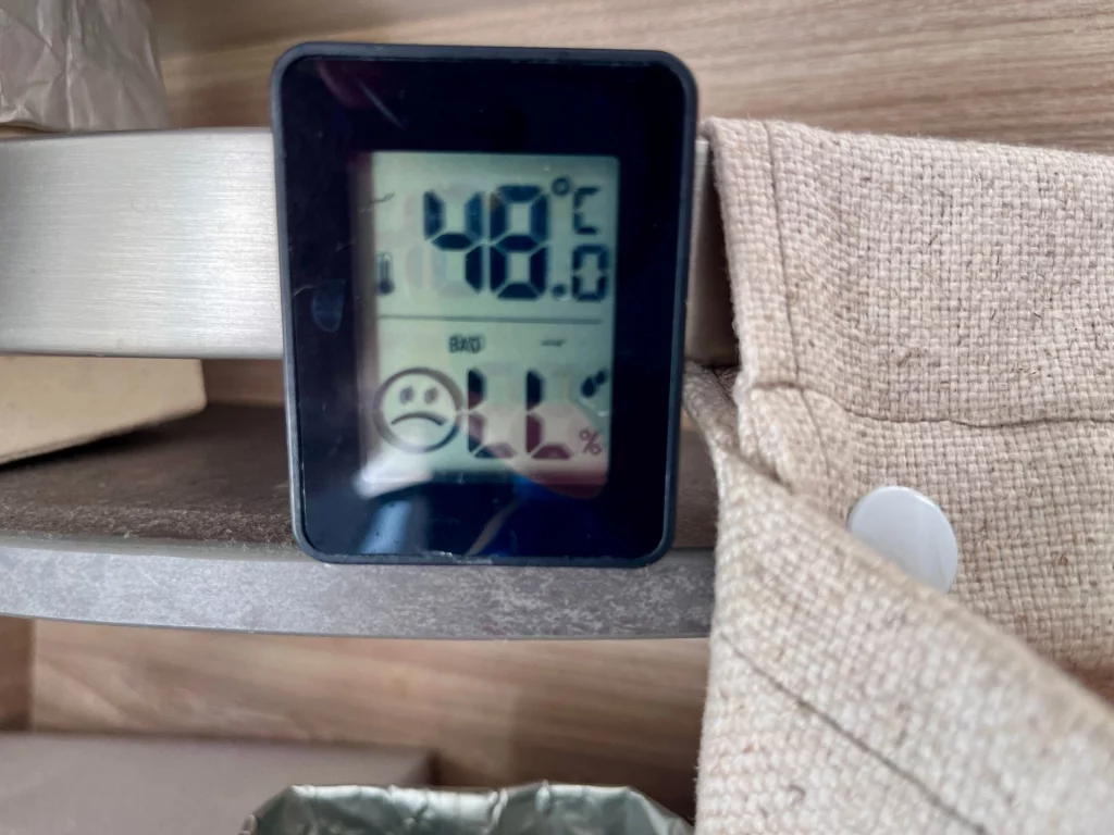 Ein digitales Thermometer im Innenraum eines Campers zeigt extreme 48 Grad Celsius und ein trauriges Smiley-Symbol für schlechtes Raumklima.
