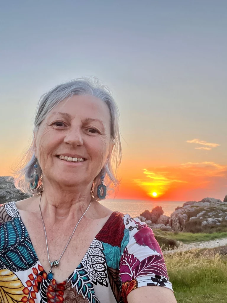 Glückliche Camperin lächelt vor einem farbenprächtigen Sonnenuntergang am Atlantikstrand bei Santander.