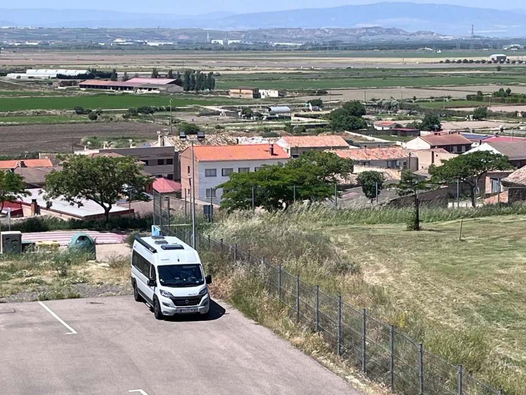Blick von oben auf den großzügigen Wohnmobilstellplatz in Valtierra mit Ver- und Entsorgungsstation und parkenden Kastenwägen.