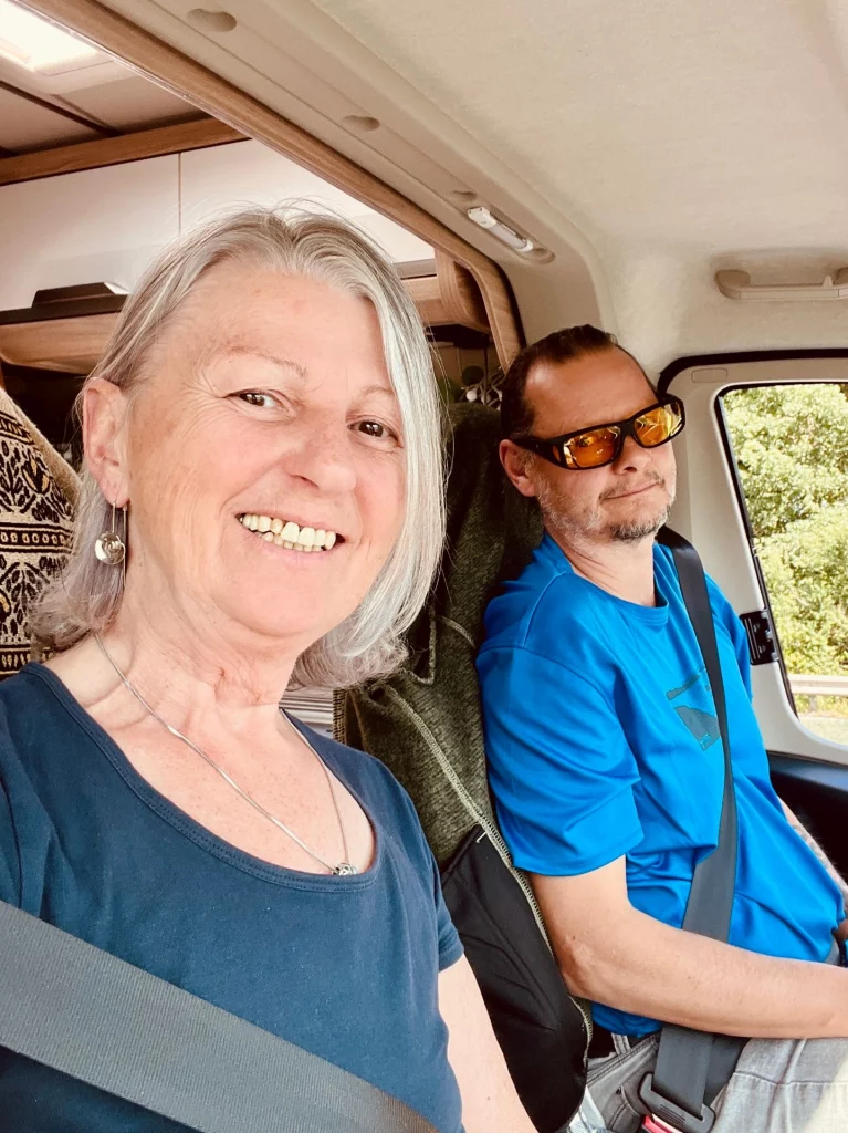 Karin und Ingo sitzen angeschnallt und gut gelaunt bei der Tankstellensuche Frankreich im Cockpit ihres Kastenwagens während eines Roadtrips durch Frankreich.