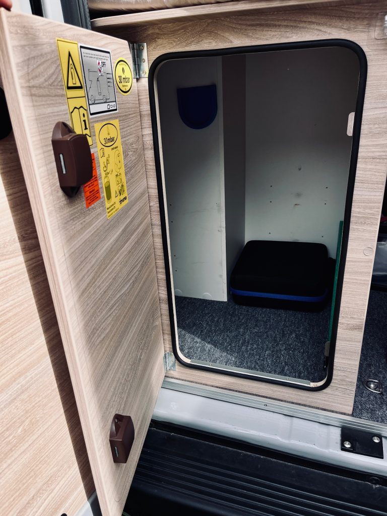Geöffneter, komplett leerer Gaskasten im Wohnmobil mit Holzoptik-Tür und freiem Stauraum.